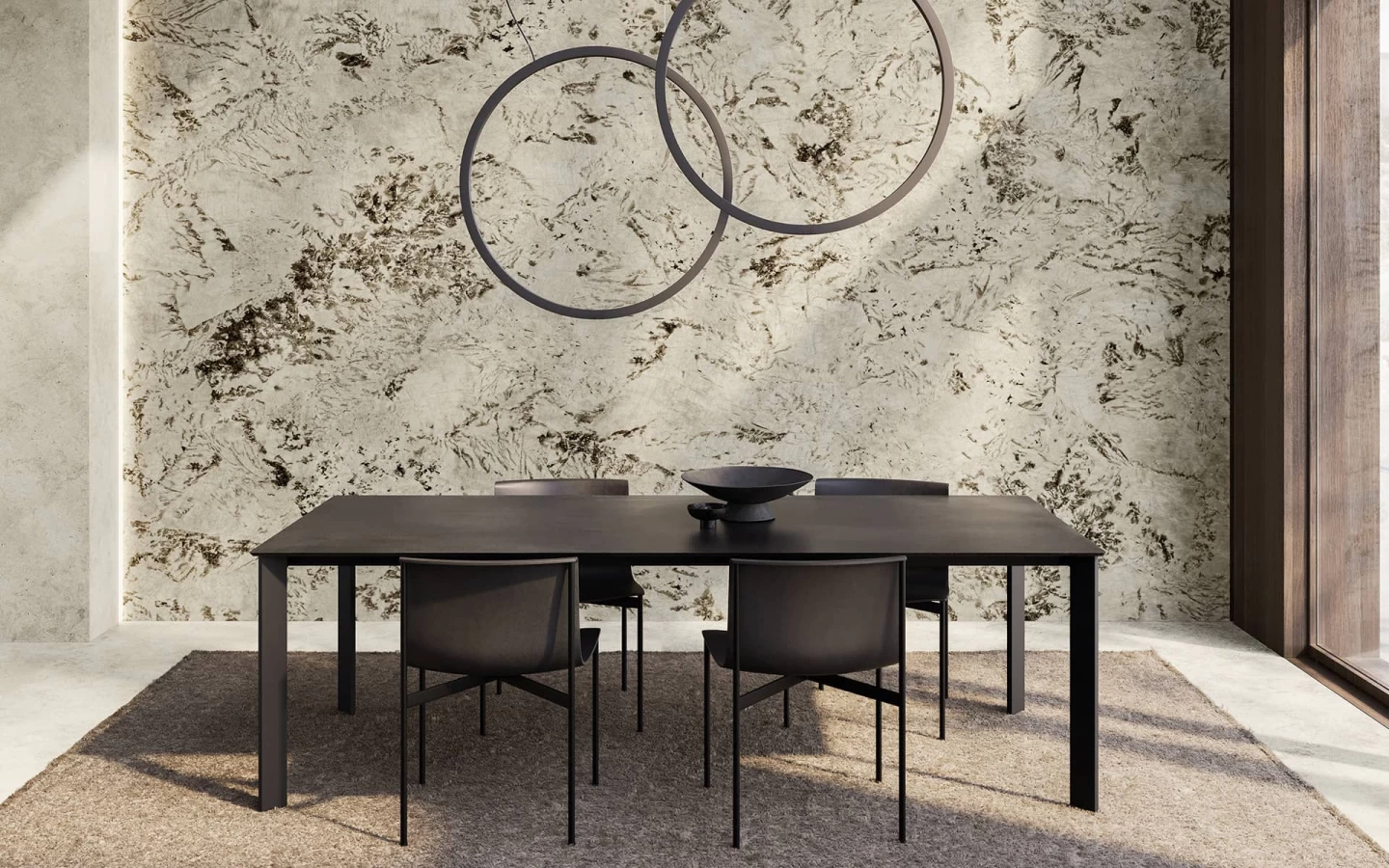 Minimalist dining table with black chairs in an open-plan space; back wall clad in Alpinus marble-effect stoneware.