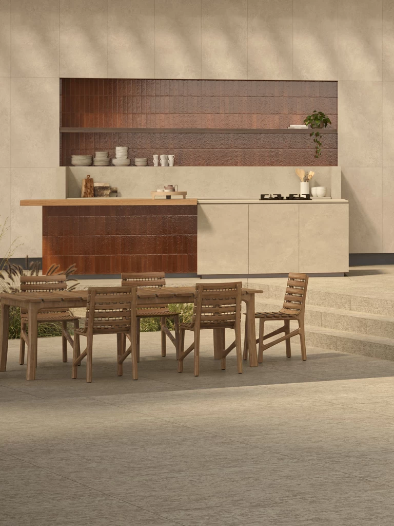 Area pranzo esterna con piano di lavoro e ante in gres effetto cemento Boost Hux Dune di Atlas Plan, abbinati a toni terracotta.