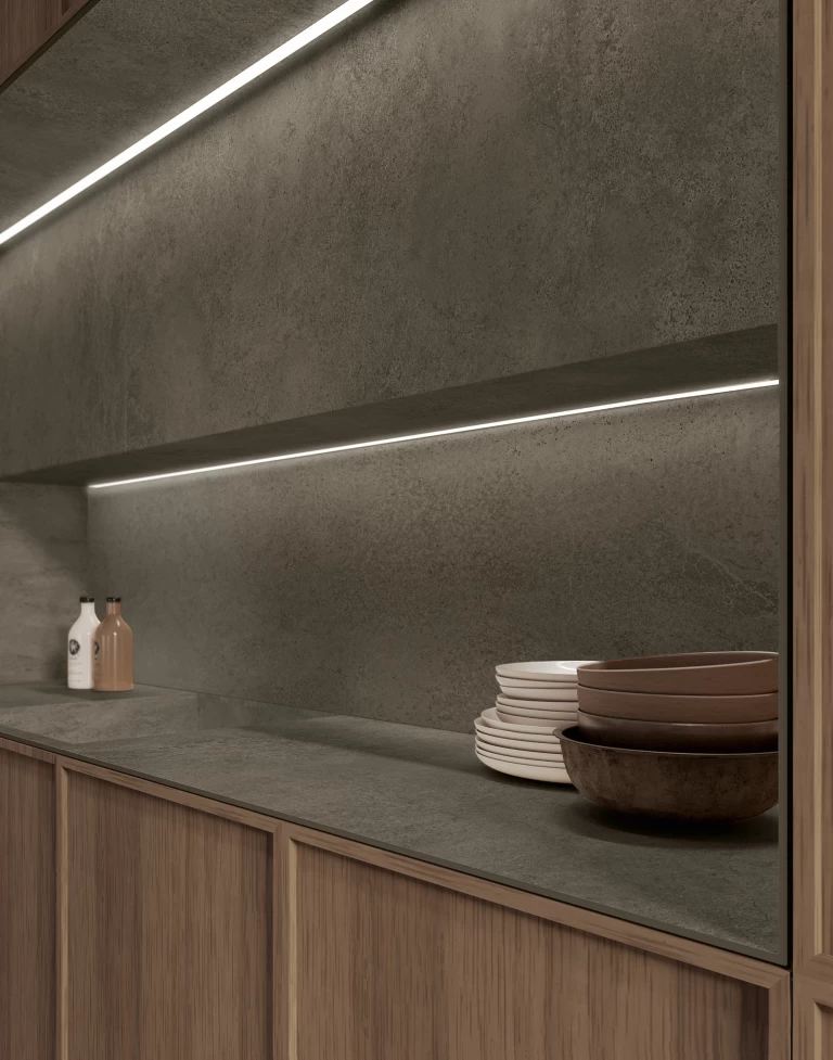 Dettaglio della nicchia retroilluminata e del piano di lavoro in gres effetto cemento Boost Hux Moka, dove la luce radente esalta la texture materica.
