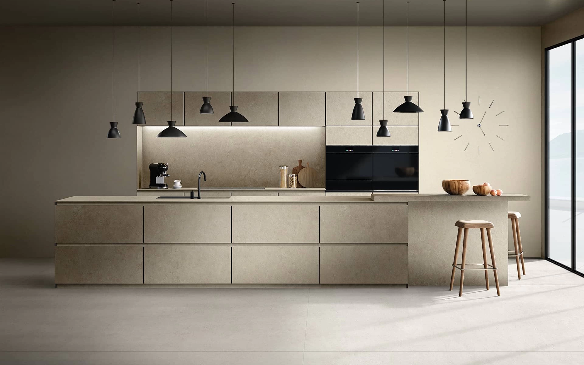 Modern kitchen with a peninsula clad in Boost Vision Camel concrete-look porcelain by Atlas Plan, illuminated by black pendant lights.