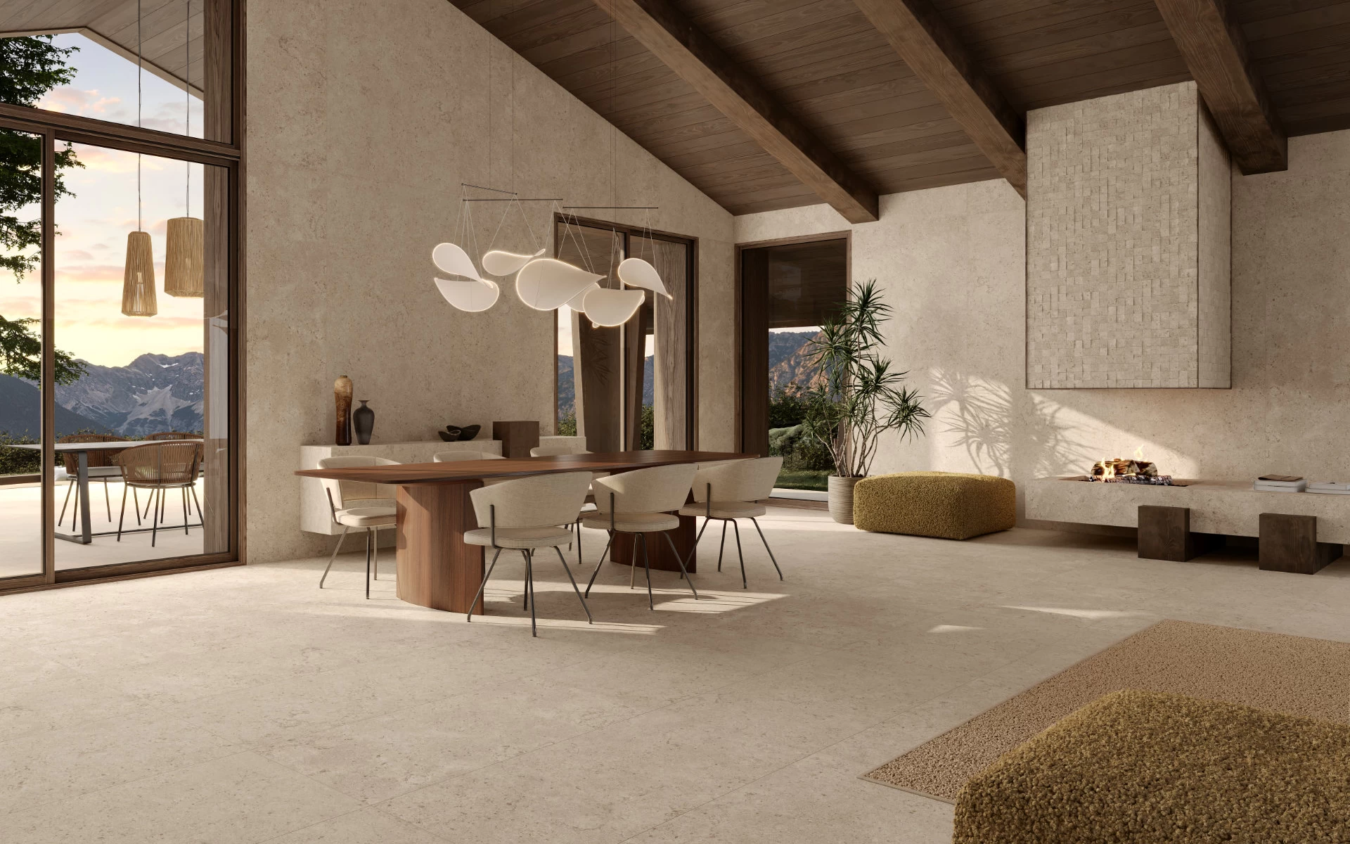 Ampio living con zona pranzo, pavimento e pareti in gres effetto pietra Nyra Utopia Barley di Atlas Plan, abbinati a travi in legno scuro e vetrate sulle montagne.