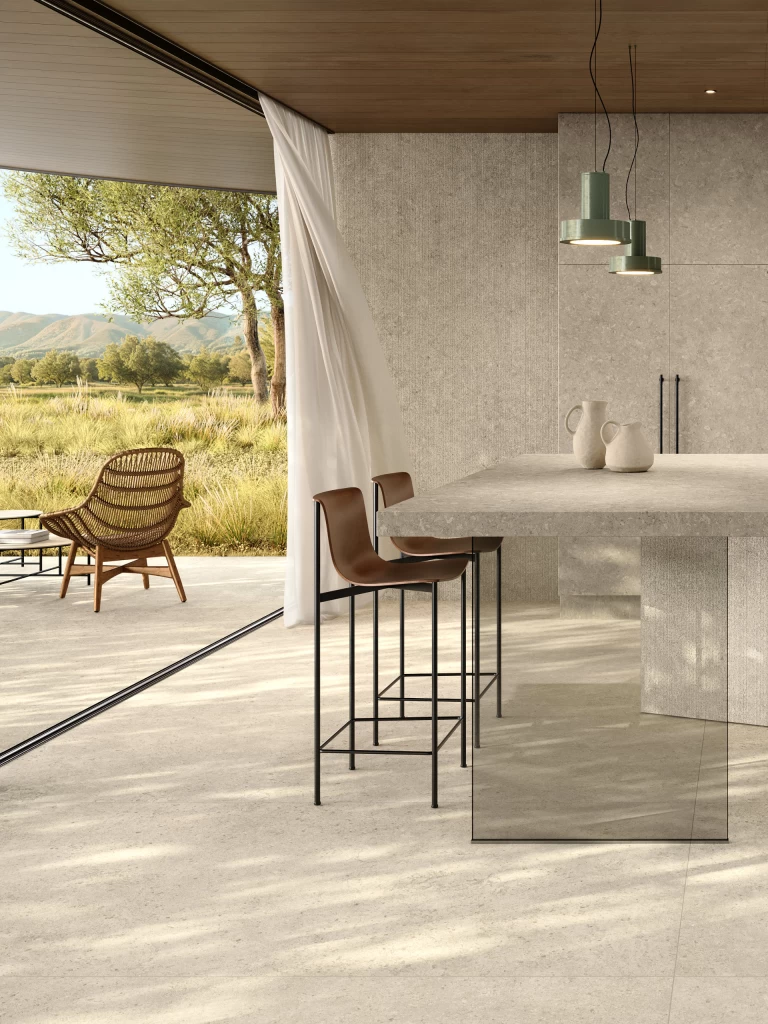 Cucina in gres effetto pietra Nyra Utopia Comet di Atlas Plan, con soffitto in legno e vista sul verde.