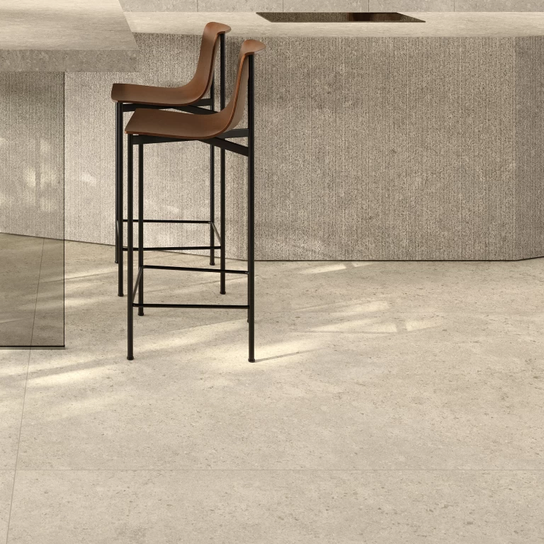 Dettaglio di cucina con isola sfaccettata, piano di lavoro e pareti in gres effetto pietra Nyra Utopia Comet di Atlas Plan, con soffitto in legno e vista sul verde.