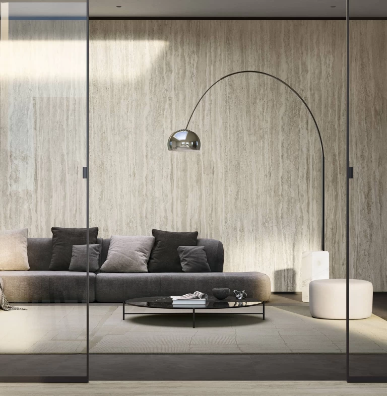 Modern living space with grey sofa and Travertino Romano Silver marble-effect stoneware cladding.