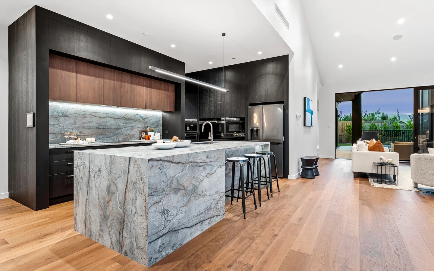 Open-plan kitchen with island in Atlas Plan Silver Root marble-effect porcelain and view of the living area