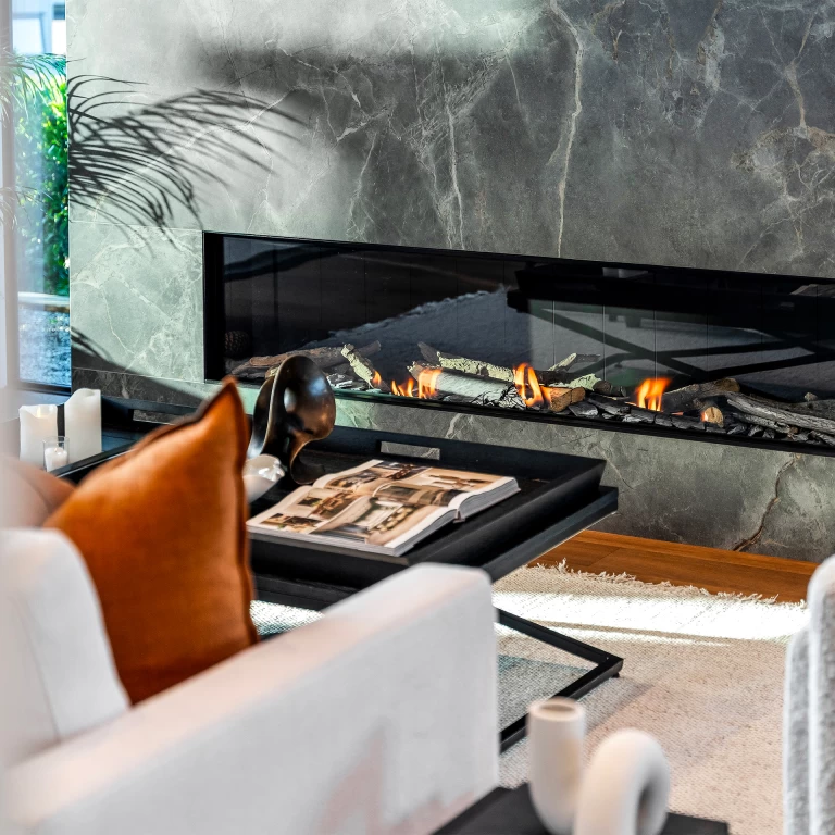 Detail of the fireplace in Atlas Plan Fior di Bosco marble-effect porcelain with lit fire