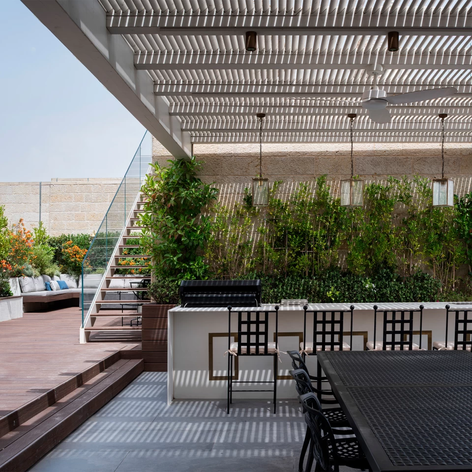 An exclusive rooftop with a kitchen island made of Atlas Plan's Calacatta Prestigio porcelain stoneware, with plants and accent lighting creating an elegant atmosphere.
