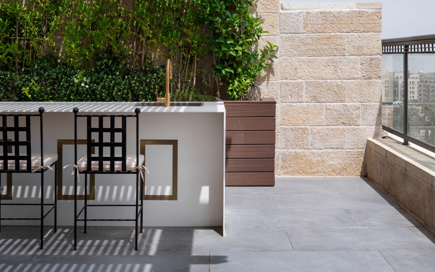 Panoramic view of a rooftop with kitchen island in Calacatta Prestigio, green wall plants and a dining area with table in a refined and cosy ambience.
