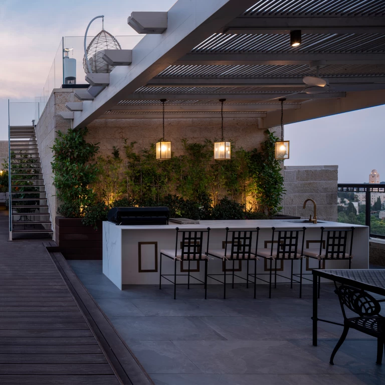 Rooftop with kitchen island in Calacatta Prestige, accent lighting and green plants that enhance the elegance and functionality of the outdoor environment.