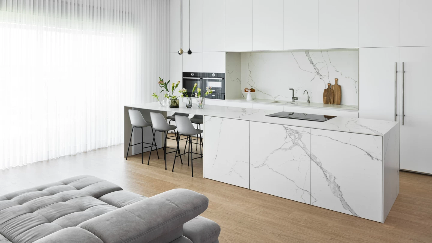 Salon spacieux avec parquet et cuisine intégrée, où se distingue le plan de travail en grès Calacatta Extra d'Atlas Plan, qui souligne la continuité entre le confort et le luxe.