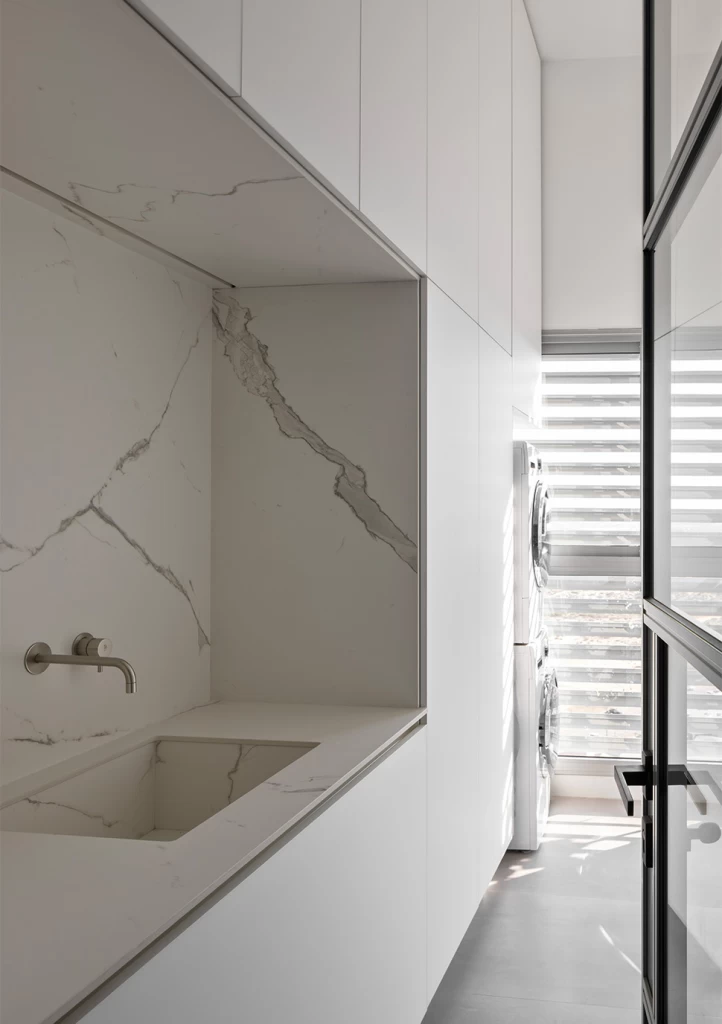 Interazione armoniosa tra la zona giorno e la cucina, dove il piano cucina in gres effetto marmo Calacatta Extra di Atlas Plan si integra perfettamente con il design moderno