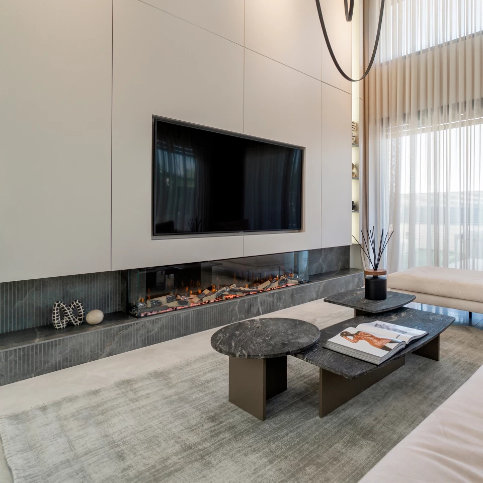 Vista de un espectacular salón con una escalera en voladizo y una pared de TV revestida de Fior di Bosco de Atlas Plan, que crea un contraste elegante y sofisticado.